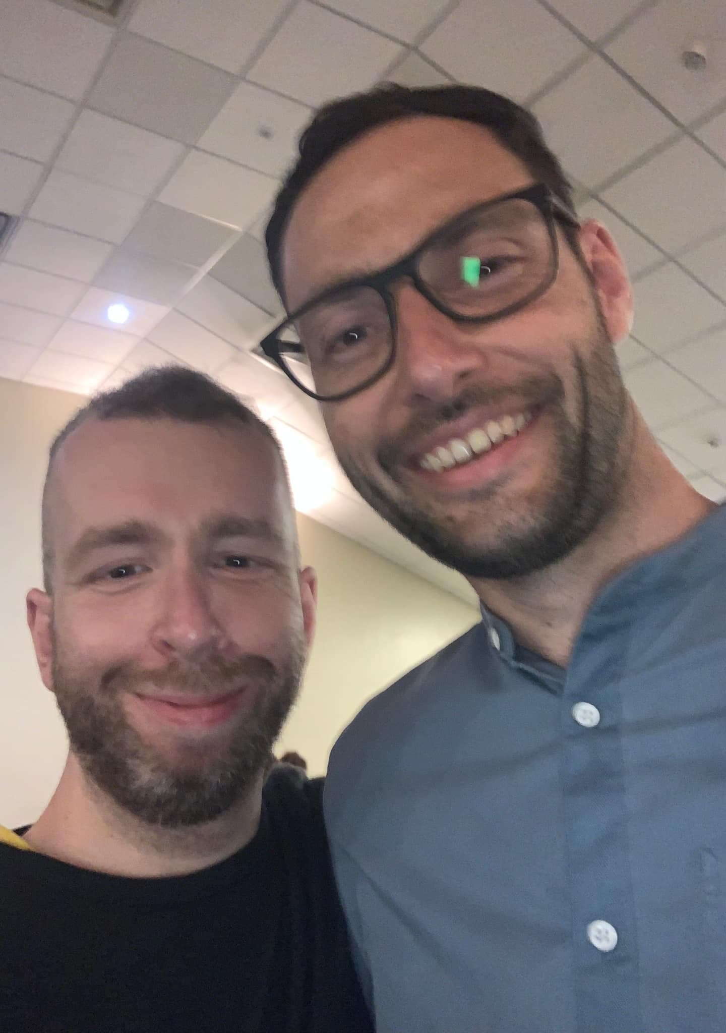 Two smiling men with beards taking a selfie, one wearing glasses and a blue shirt.