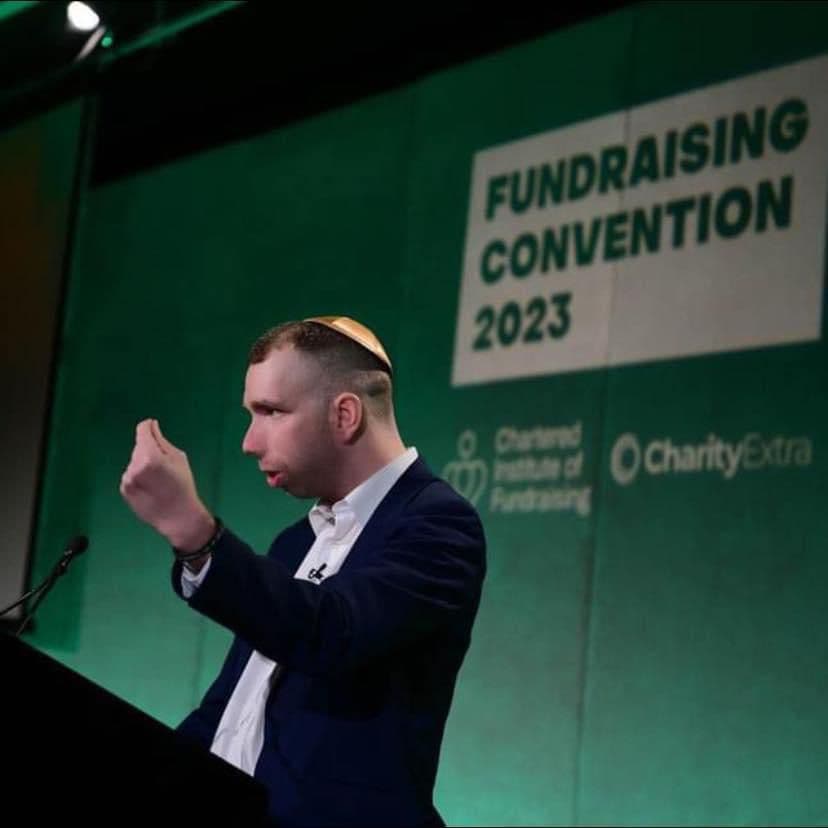 Man in a suit and kippah gestures while speaking at the Fundraising Convention 2023.