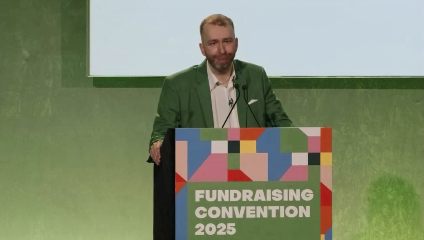 Man in a green blazer speaking at a colorful Fundraising Convention 2025 podium.